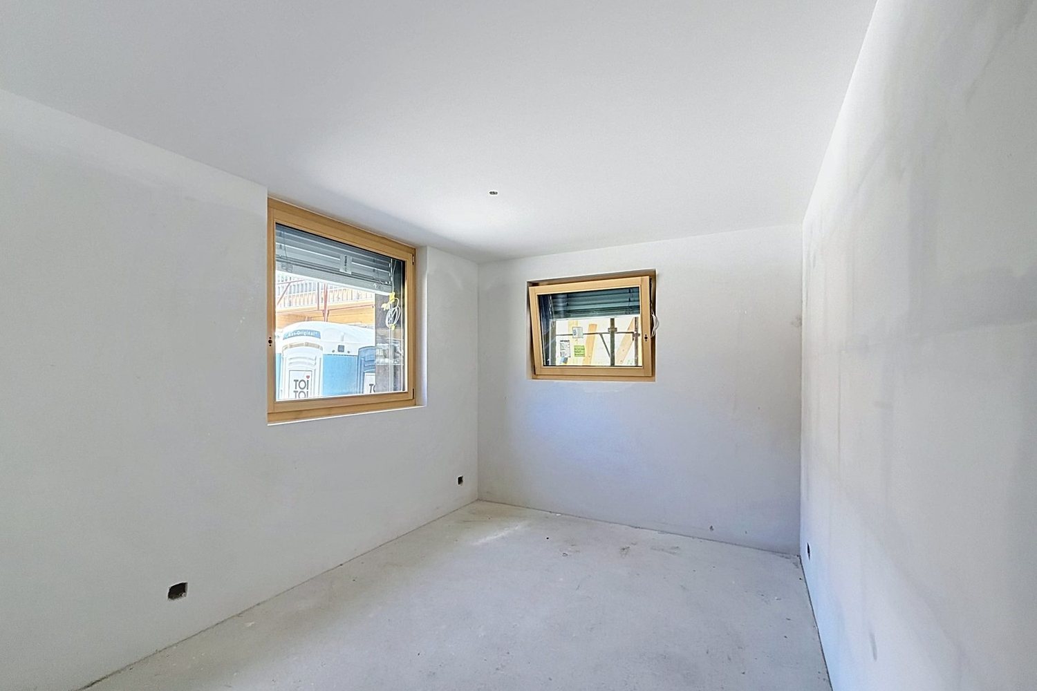 Une chambre en cours de finition : plâtrerie réalisée, deux fenêtres en bois posées.