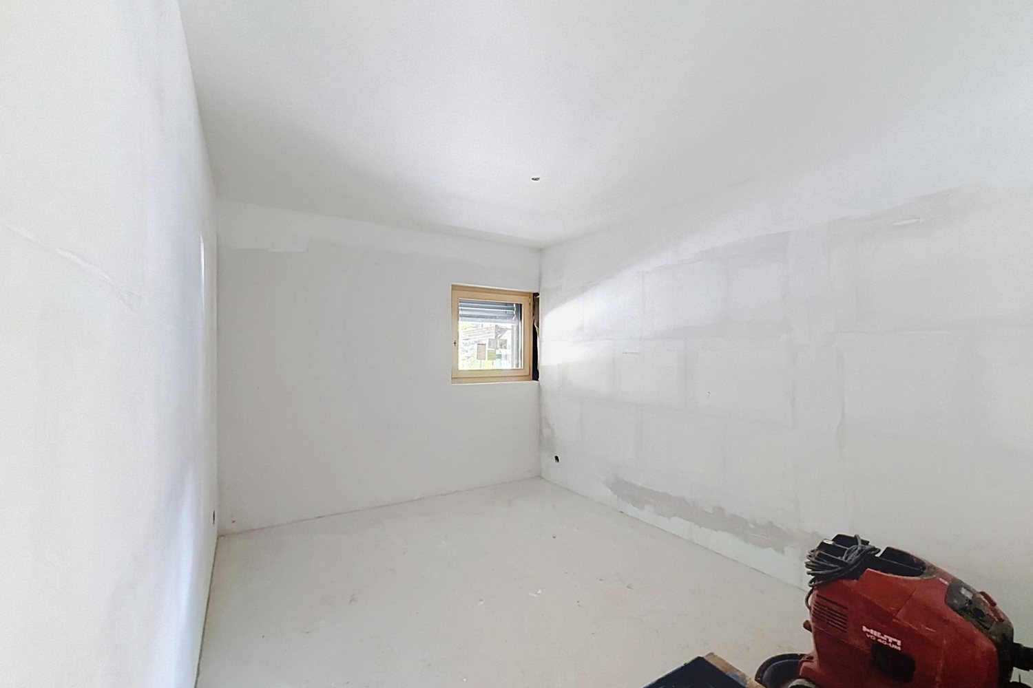 Une chambre en gros œuvre, fenêtre en bois posée, murs prêts pour la finition.